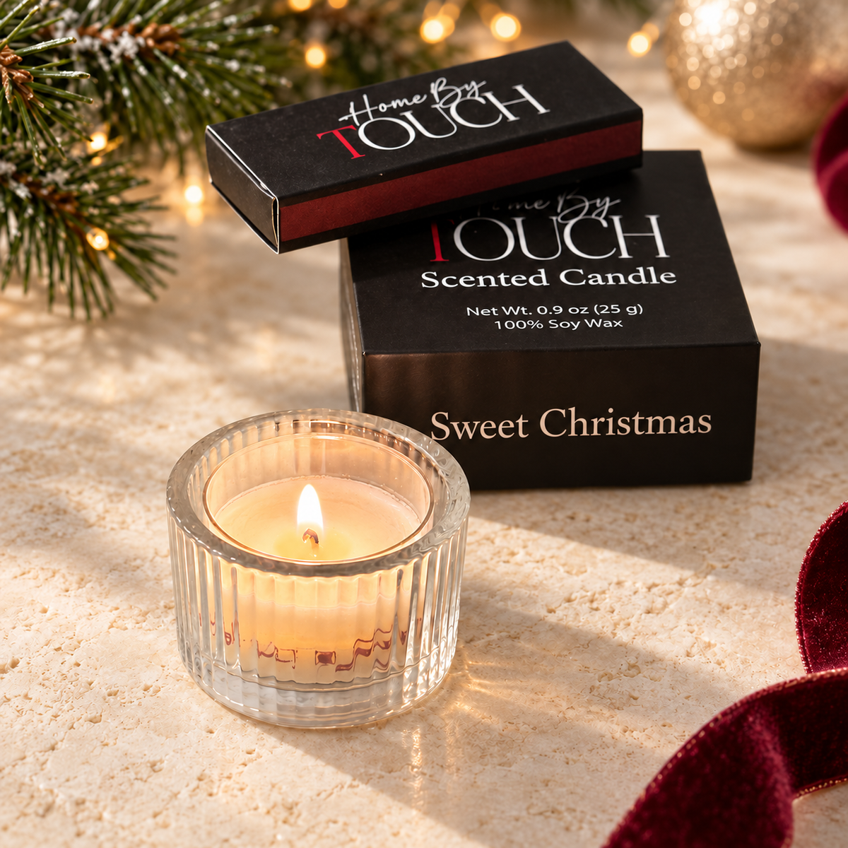 Sweet Christmas tea light in a clear ribbed glass holder beside its black Home By TOUCH sample box and luxury matches, styled with evergreen.