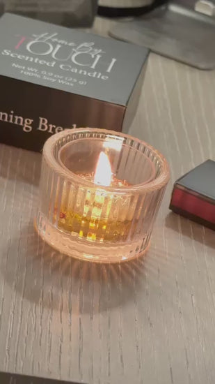 A lit Home By TOUCH tea light in a ribbed glass holder, with Morning Breakfast packaging and luxury matches.