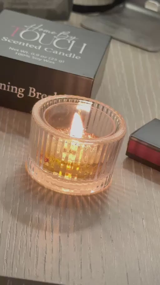 A lit Home By TOUCH tea light in a ribbed glass holder, with Morning Breakfast packaging and luxury matches.